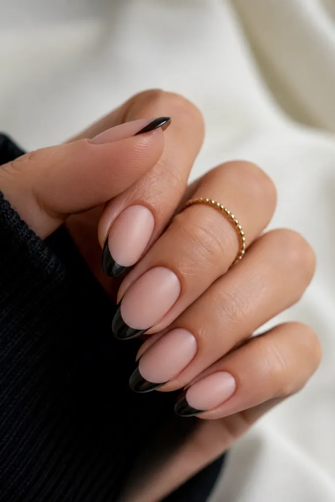 Matte nude nails with sharp glossy black French tips. The smile line is clean and the black tip is glossy like lacquer.