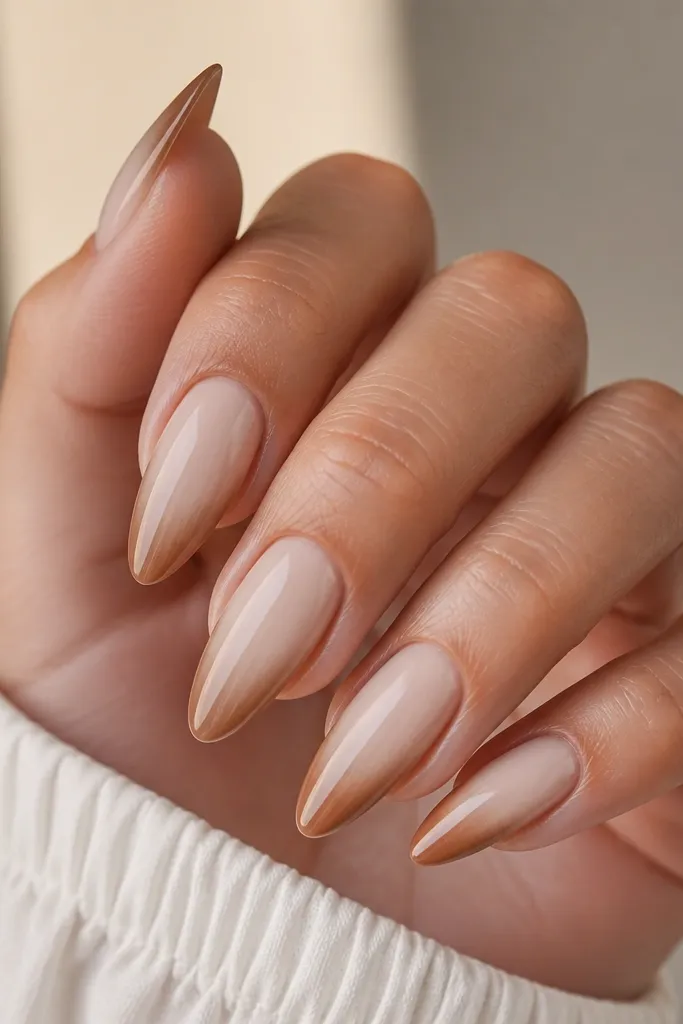 Long almond nails with a creamy nude base. Tips fade from light brown at the outer edge to almost nude near the smile line, creating a soft gradient.