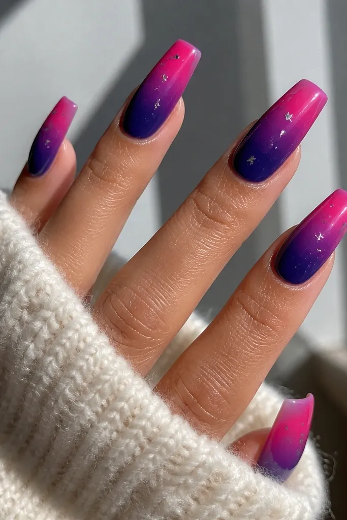 Coffin nails with a dramatic gradient: indigo blue at the cuticle fading to hot pink at the tips. The ombre is smooth and glossy, with tiny silver star specks scattered near the pink area.
