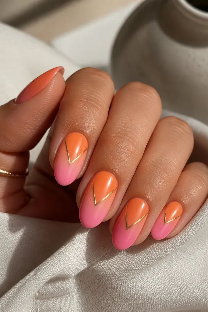 Medium oval nails with an ombre from orange near the cuticle to sherbet pink at the tips. Each nail has a thin V-shaped horizon line pointing toward the center, drawn in warm gold.
