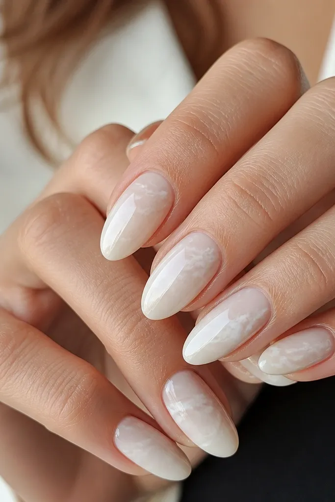 Almond nails with a smooth almond-white base. Thin milky white marble veins run diagonally, with a few slightly thicker swirls. Glossy top coat, marbled look is airy, not heavy.