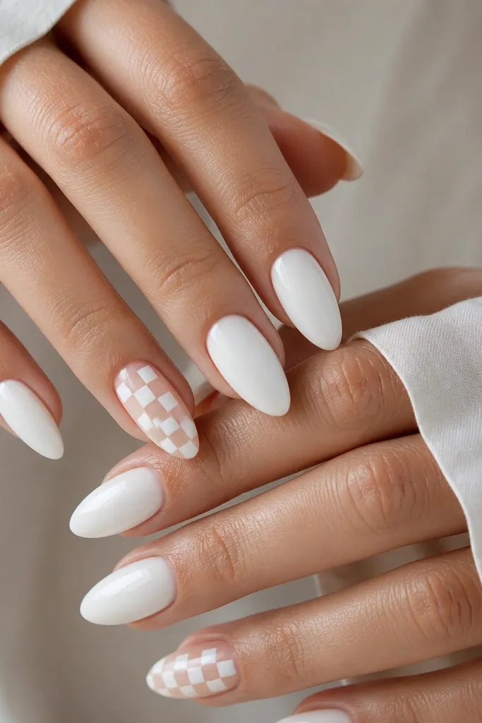 Most nails are almond white solid with glossy finish. Two accent nails have a tiny checkerboard pattern in milky white on a nude base near the center, with clean square edges.