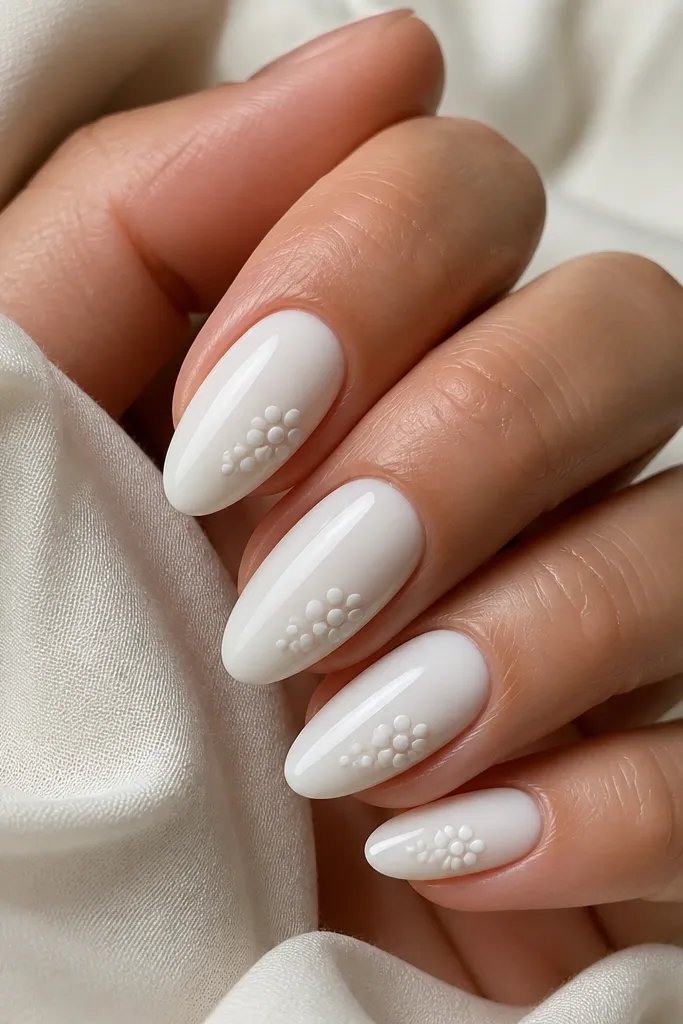 Almond nails in almond white. On each nail, there's a cluster of milky white dots arranged like a small flower near the side of the nail, with a few dots slightly larger. Glossy finish.