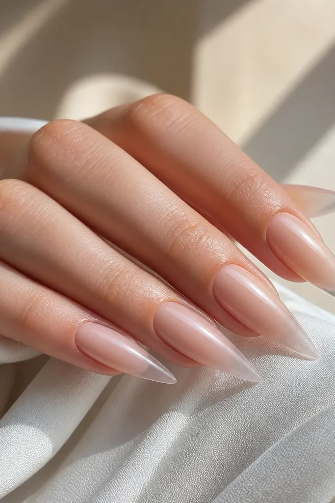 Stiletto nails showing a nude ombre that fades into a clearer, more translucent tip; the free edge looks lighter and slightly see-through, with a glossy finish.