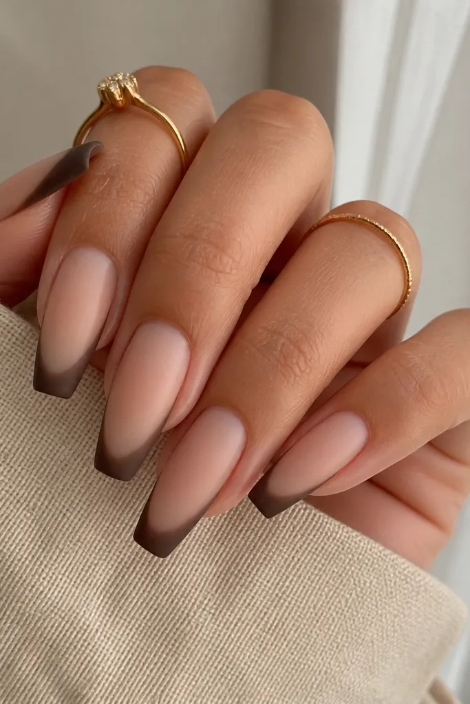 Coffin nails in a sheer nude base with mocha brown French tips. The brown looks matte or velvety, and the edge of the French line is slightly softened, not razor-straight.