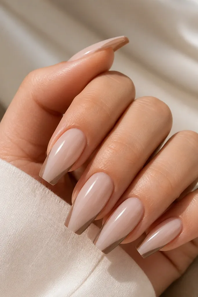 Coffin nails with milky nude base. The French tip is milk tea brown on the sides, but there's a small negative space triangle in the center near the free edge. Glossy finish.