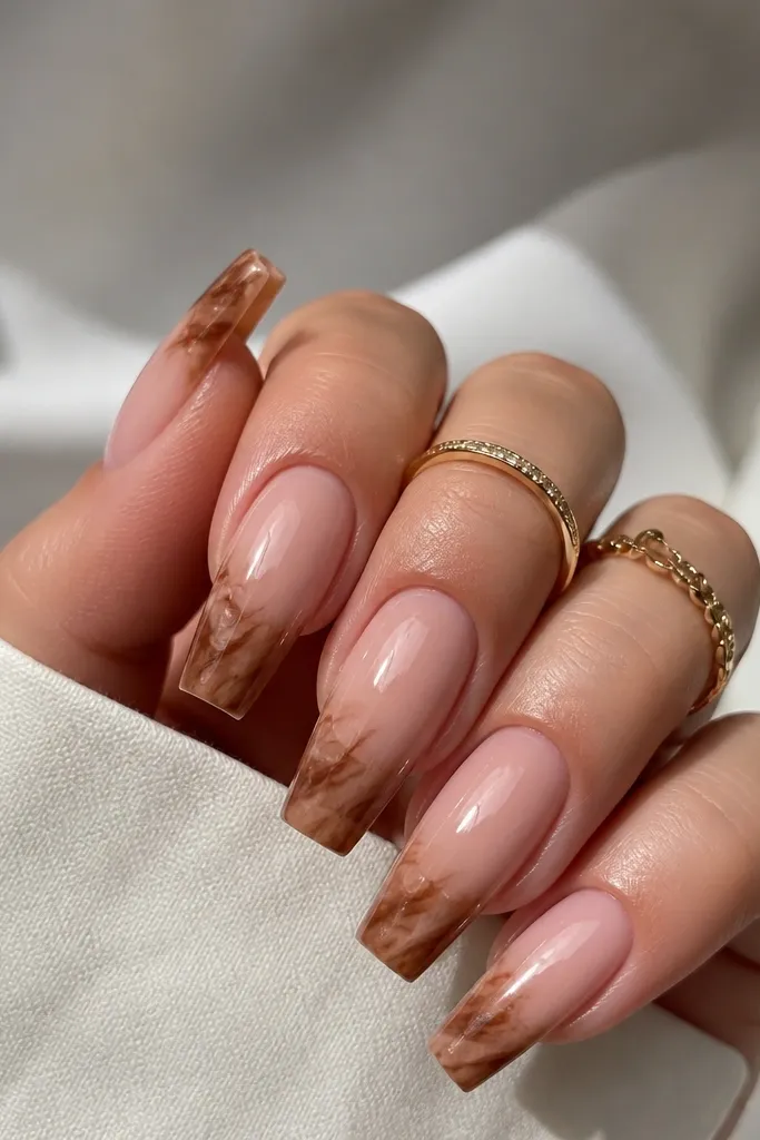 Coffin nails with sheer nude base. The French tip region has a caramel-brown marble effect with thin wispy lines, glossy finish, and the free edge still looks structured.