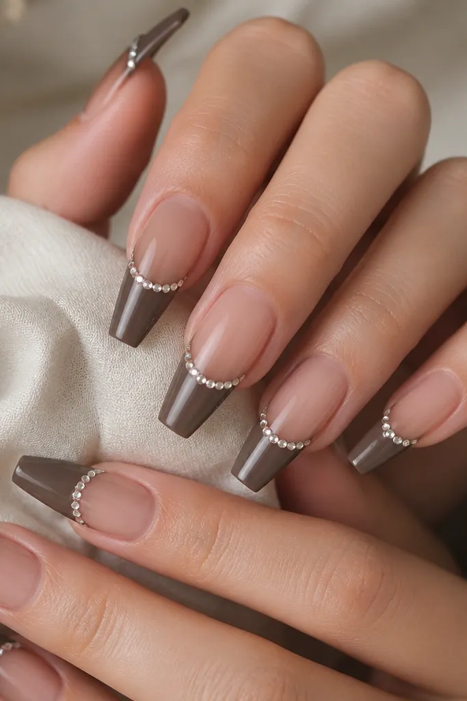 Coffin nails with sheer nude base. French tips are dark taupe brown and glossy. A tiny row of single rhinestones sits along the top edge of the French line on each nail.