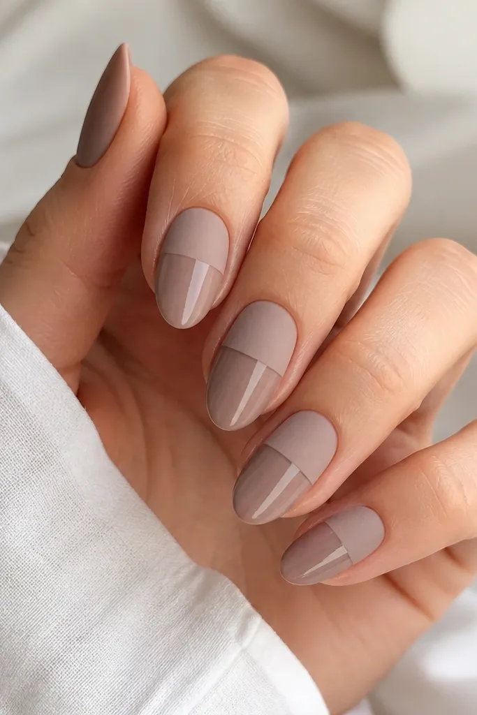 Short almond nails in taupe nude. The base is glossy at the bottom half, and the top half is matte, separated by a clean horizontal line. Crisp edges.