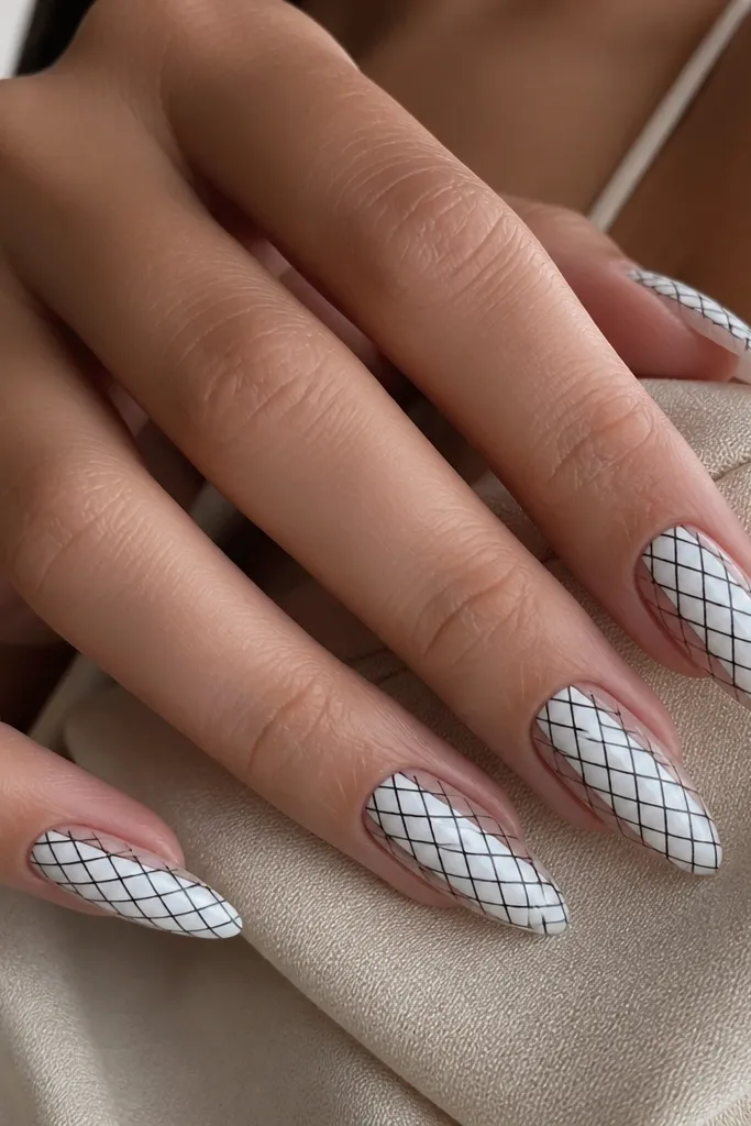 White almond nails where only the center is painted white; the sides show negative space. Black lines form a tight crisscross net pattern across the nail.