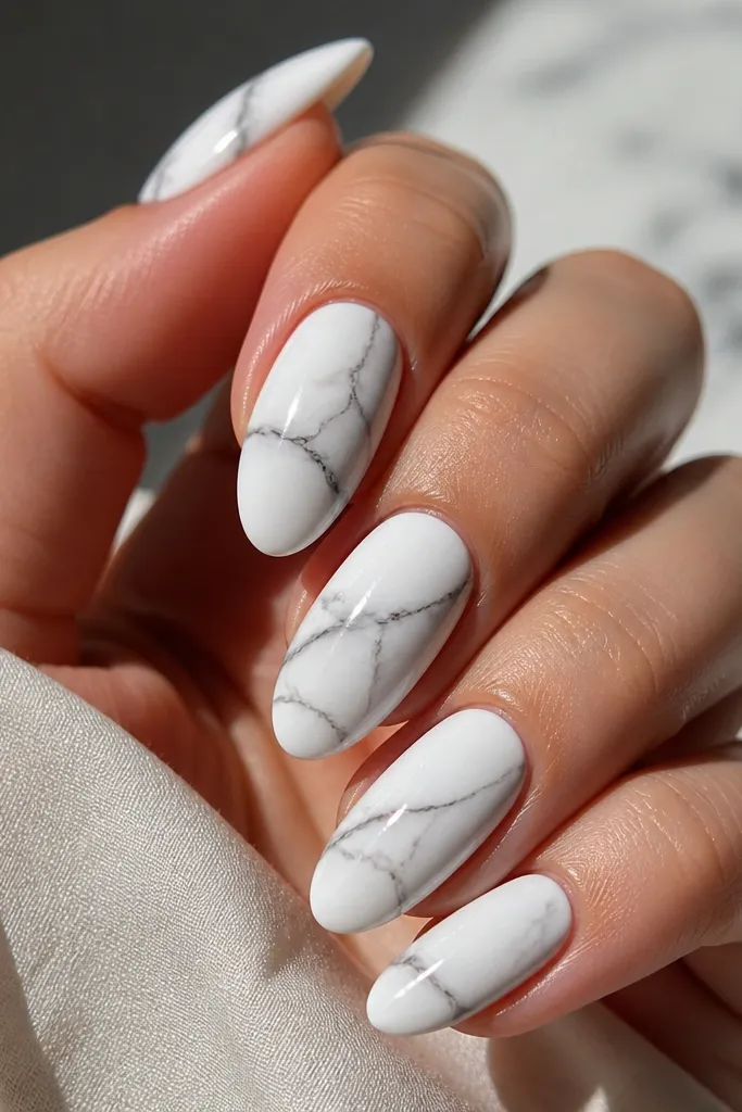 Glossy white almond nails with thin black marble veins. The veins curve like natural stone, with a soft fade where black thins out.