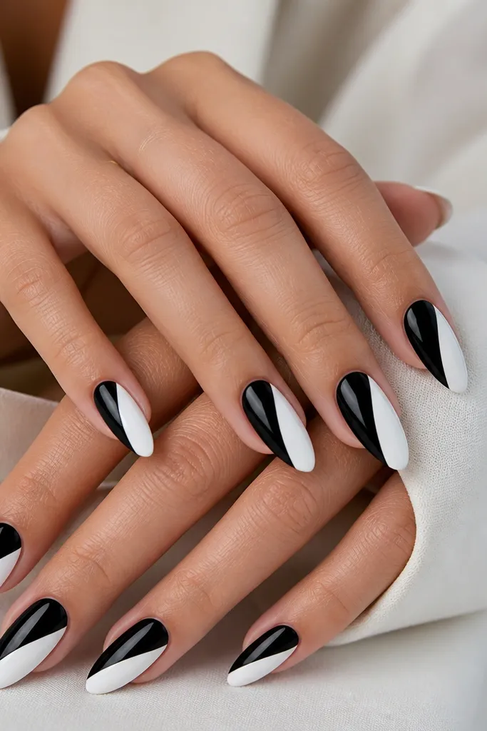 Almond nails with diagonal stripes: one side is solid black, the other is solid white, separated by a sharp diagonal line. The finish is glossy and clean.