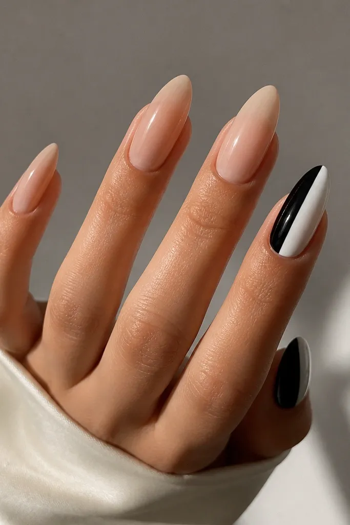 Almond nails where the left side is bare natural (clear nude) and the right side is split between black and white. The seam is straight and glossy.