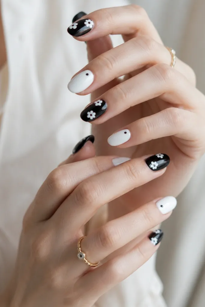 A mix set: some nails are glossy black with tiny white five-petal flowers and black centers. Other nails are clean white with a single small black dot near the cuticle.