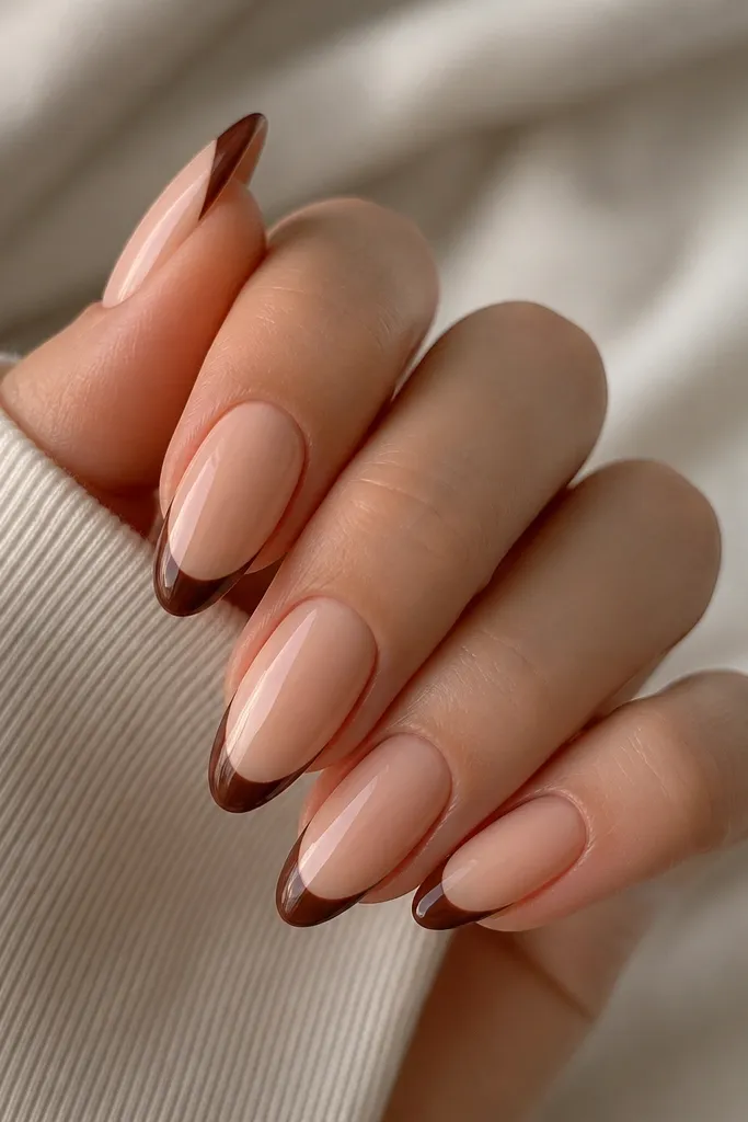 Almond nails with a nude base. A chocolate brown French tip is outlined with a very thin line in a lighter nude-brown along the inner edge.