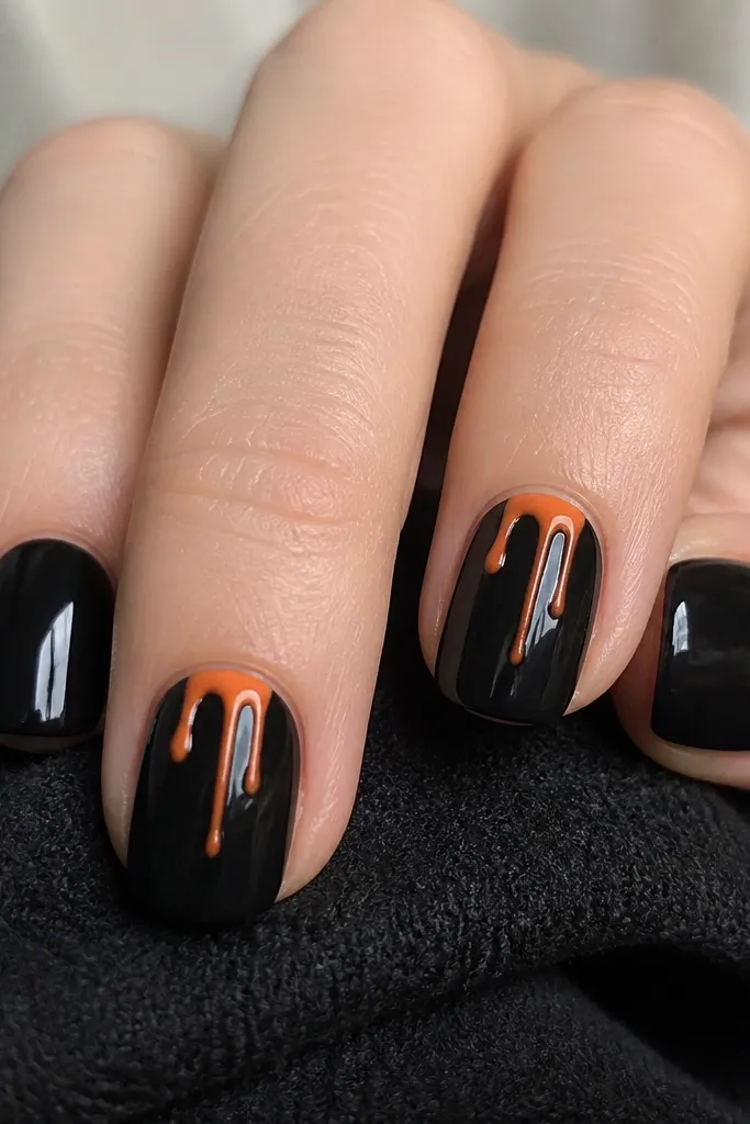 Short nails with a glossy black base. On two nails, orange drips slide from near the cuticle down toward the center, tapering as they go. The drips look like melted candle wax. The other nails are plain black.