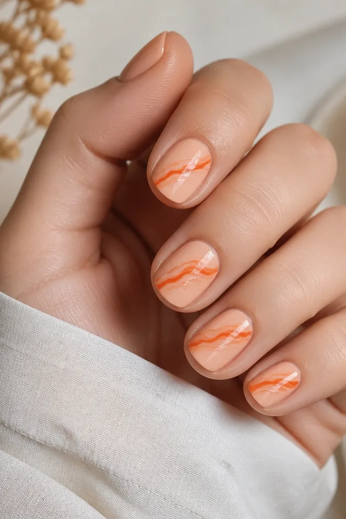 Short nails with a peach base. A small marble swipe pattern crosses the center: orange and burnt orange streaks with thin milky lines. Glossy top coat makes the swirls shine.