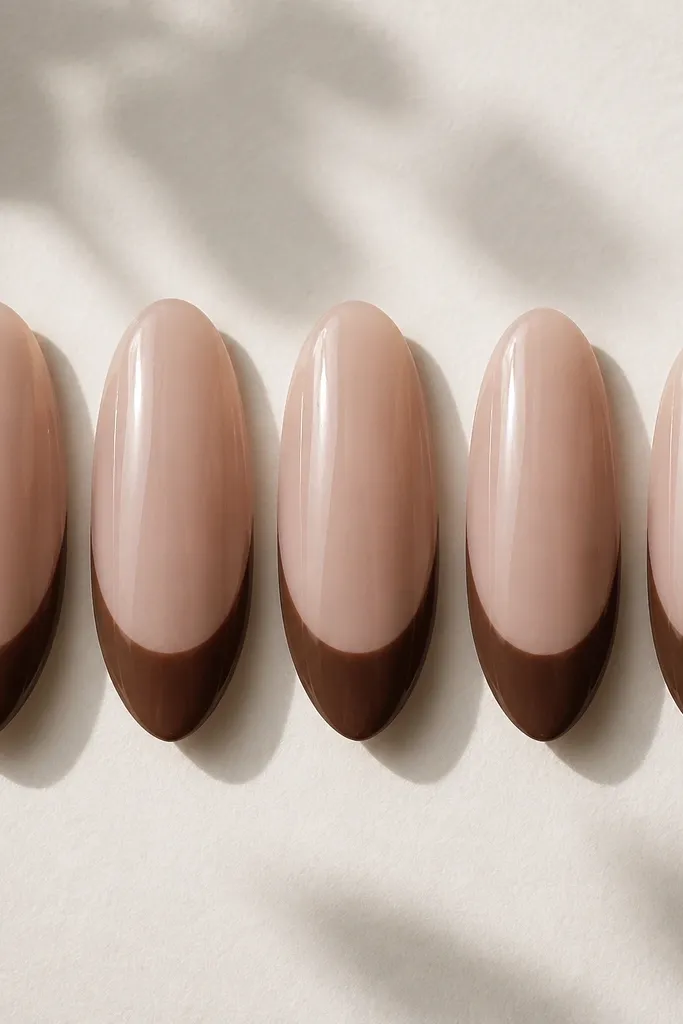 Five almond nails shown straight-on. The base is a sheer pink-beige (latte) with a smooth nude glow. The french tips are a clean chocolate brown arc, medium width, with sharp edges and a glossy topcoat.