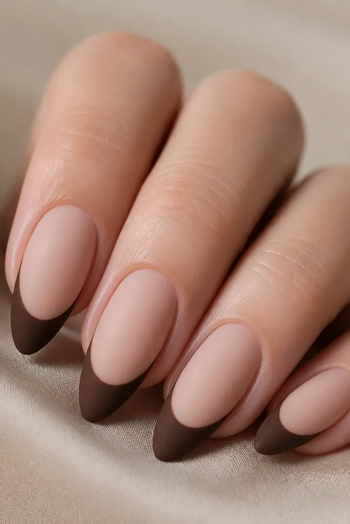 Close-up of four almond nails. The base is nude blush and slightly creamy. The french tips are chocolate brown but completely matte, with a soft velvety surface and no shine.