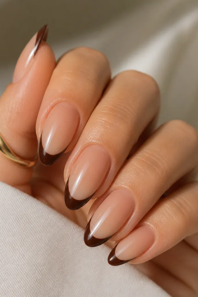 Five almond nails with a base that fades from slightly darker near the cuticle to lighter toward the free edge. The french tips are chocolate brown and glossy with crisp arcs.