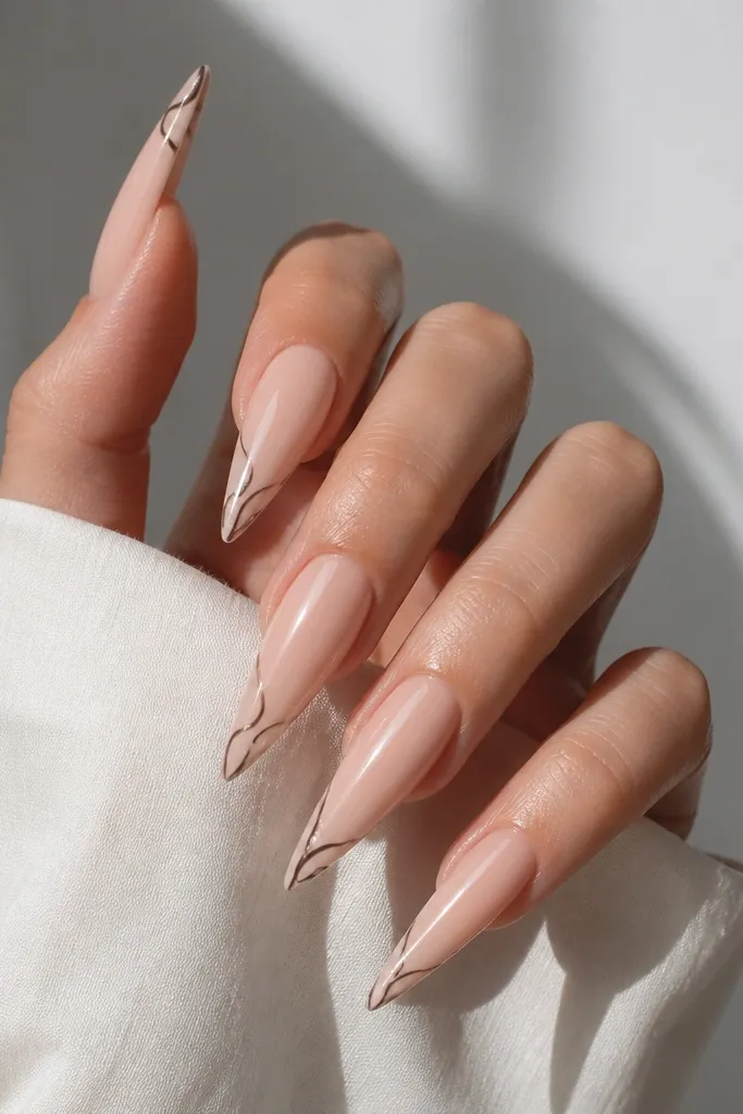 Long stiletto nails in glossy nude. At the very tip, there's a thin black-brown swirl line art, delicate and minimal.