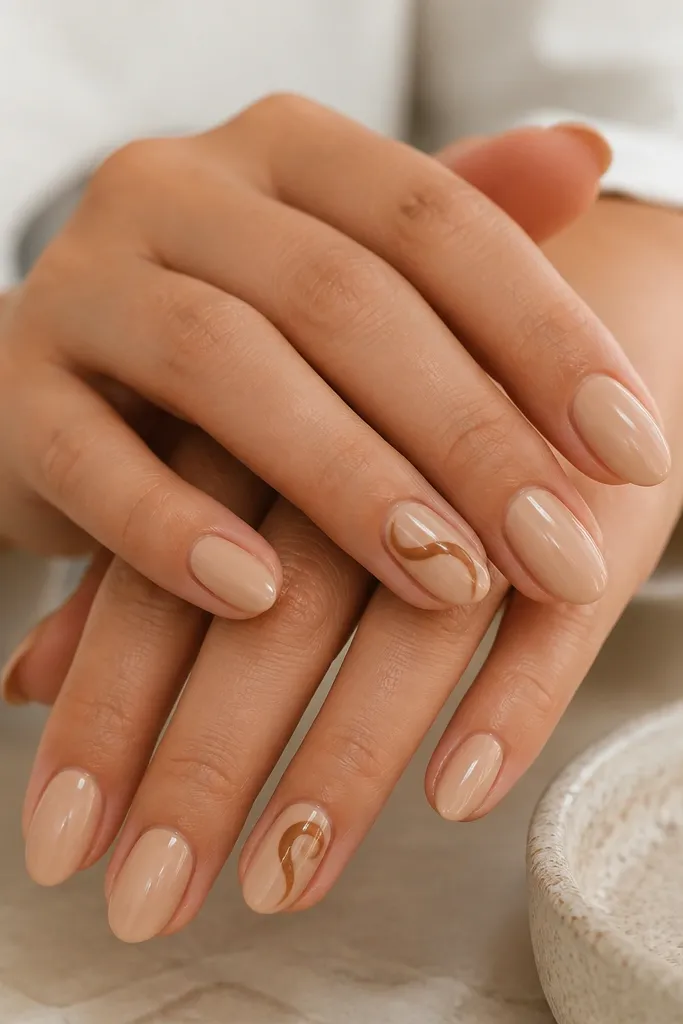 Short almond nails painted warm nude. Two accent nails have a thin caramel-brown swirl starting near the center and curling toward the tip. The swirl lines are smooth and slightly thicker in one spot, with glossy shine overall.