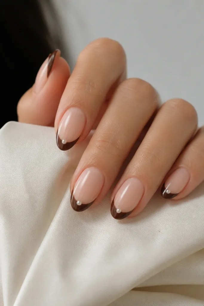 Medium nails with a nude base. Deep brown French tips. One tiny pearl dot sits at the center of each tip.