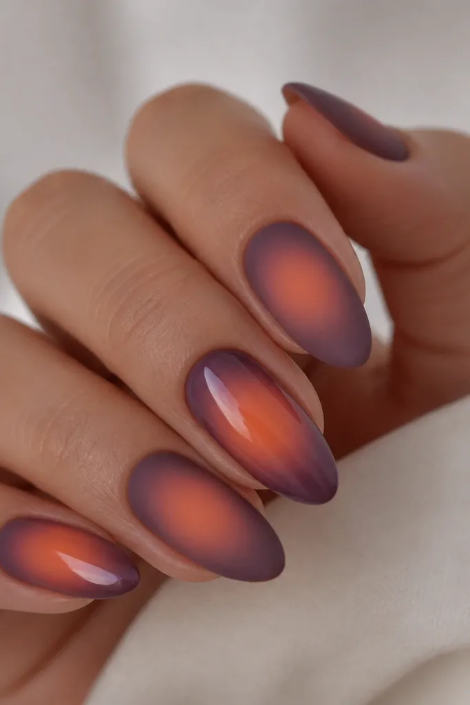 A set where most nails are matte purple smoke aura with a soft orange glow in the center. One or two nails are glossy, with the orange center glowing brighter under shine.