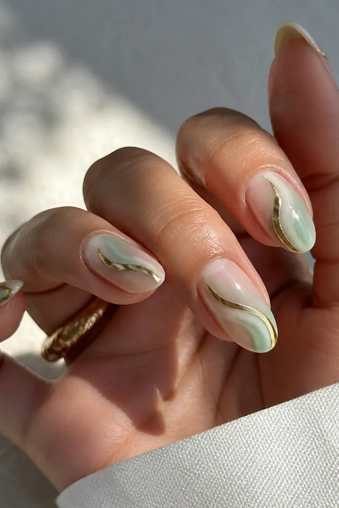 Nails with a translucent jade tint over a clear base. A gold chrome swirl runs diagonally across each nail, with the swirl edges crisp and reflective.