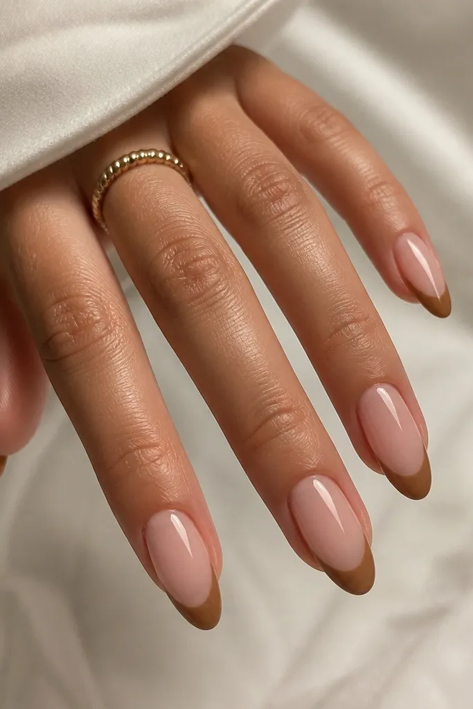 Almond nails with a nude pink base. The French tip is caramel brown with a slightly curved "smile" line, filled softly toward the center, glossy top coat.