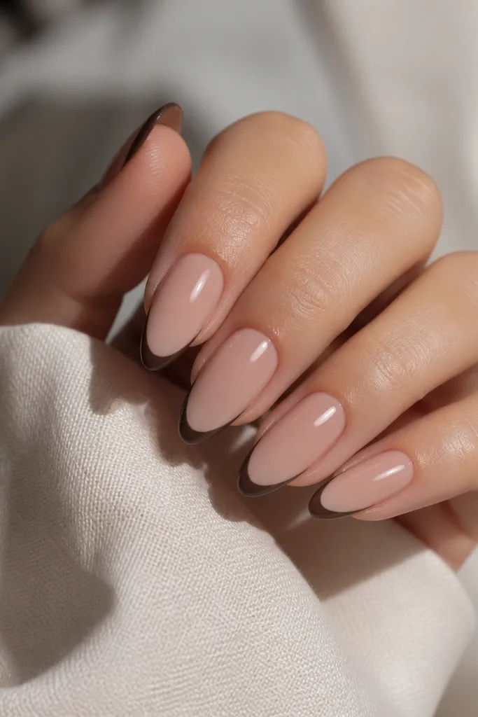 Almond nails with glossy sheer nude base. The French tips are matte chocolate brown, clean and thin, with a slight contrast between matte tips and shiny base.