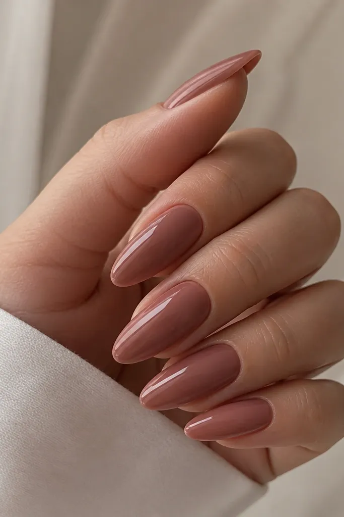 Almond nails in a rosewood nude, slightly deeper than a typical pink-beige. The surface looks like glass - ultra reflective, no art, no pearls, no stripes. Cuticles are clean and blended.