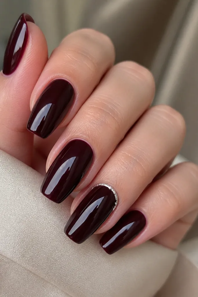 Five short coffin nails painted black cherry with a high-gloss glazed shine; one accent nail has a thin silver half-moon near the cuticle.