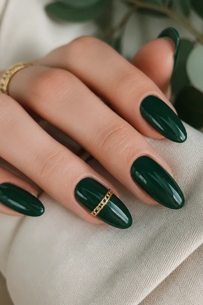 Deep green glossy nails with one accent nail showing a tiny gold chain link across the middle, like jewelry on the nail.