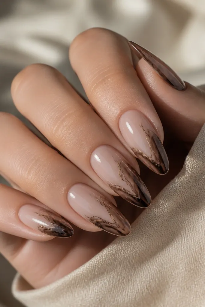 Almond nails with a sheer nude base and a chocolate marble pattern concentrated on the French area. Fine brown chrome veins run through the marble like hair-thin highlights. High gloss, soft swirls.