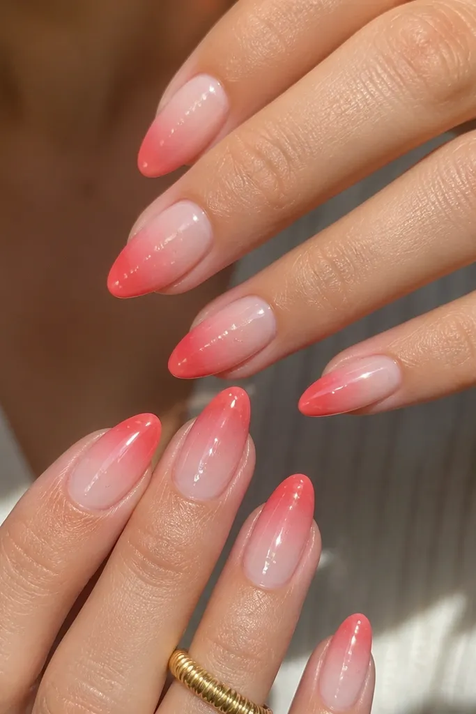 Medium almond nails with a clear jelly middle and a coral-pink sunrise fade concentrated at the tips. The center looks see-through and glossy, with tiny suspended shimmer in the jelly.