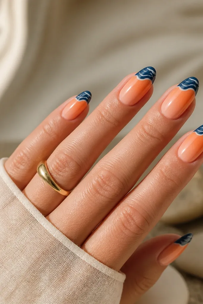 Gradient nails that start peach and fade into orange, then a navy wave edge sits at the very top of the tip. Thin white wave lines run through the navy area.