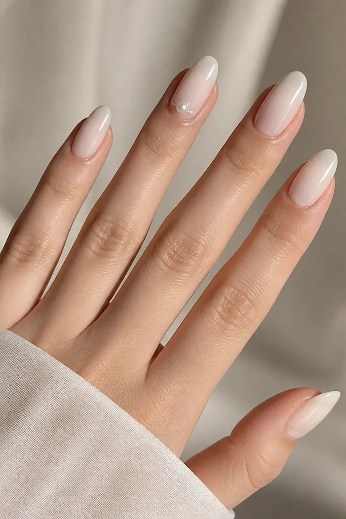Almond nails in sheer milky white. Only the ring finger has a single small pearl placed near the cuticle with a tiny glossy drop around it.