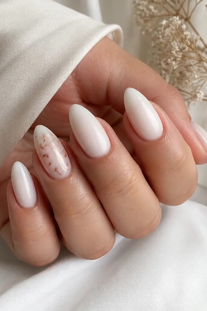 Milky white almond nails with one accent nail showing scattered rose gold foil flakes near the center, mostly translucent and not fully covered.