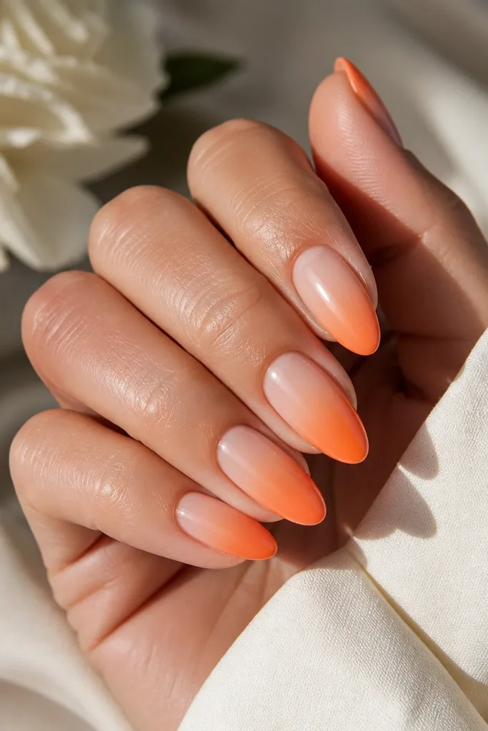 Medium almond nails with a milky peach base. Tangerine ombre starts around the middle of each nail and fades toward the tip, leaving the cuticle area bare and clean. High-gloss finish.