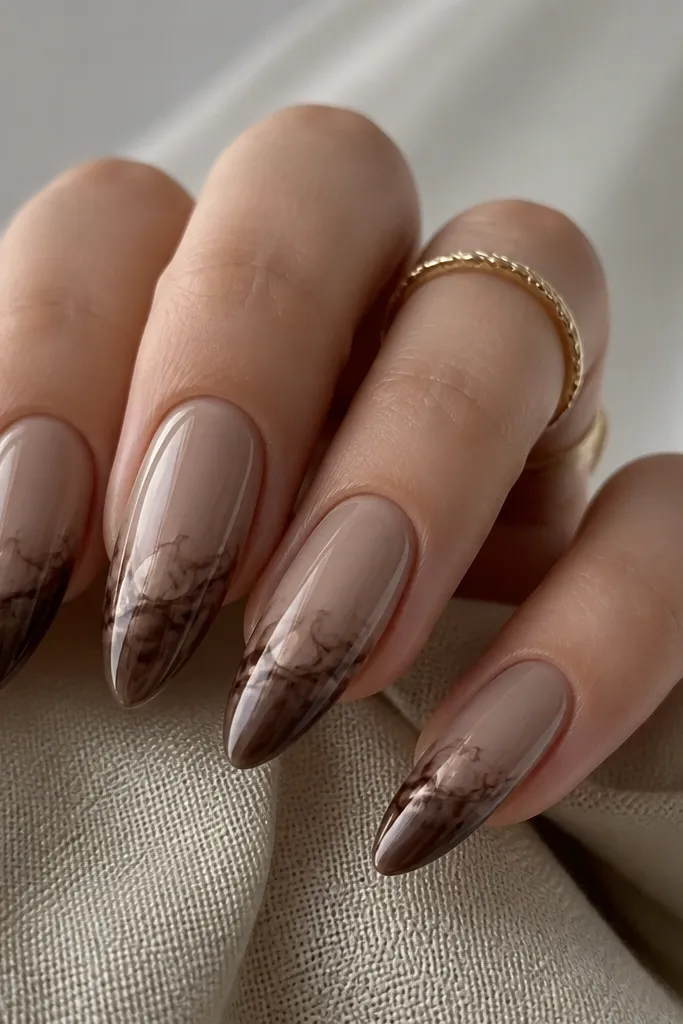 Long almond nails. Base is sheer taupe. Tips are deep brown. The chrome effect looks like a smoky marble at the edge - taupe chrome swirls that fade into the brown like smoke.