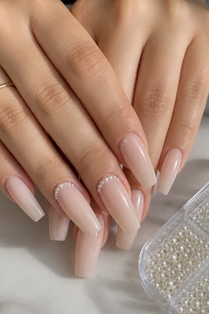 Coffin nails in milky nude, semi-opaque and glossy. Two nails on each hand have small white pearl dots placed right at the cuticle line, with a pearl storage tray shown in the corner.