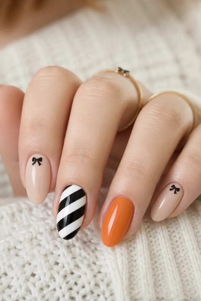 Alternating thick diagonal stripes in black and white on two nails, with a single orange stripe nail. The rest are glossy nude with a tiny black bow sticker near the cuticle.