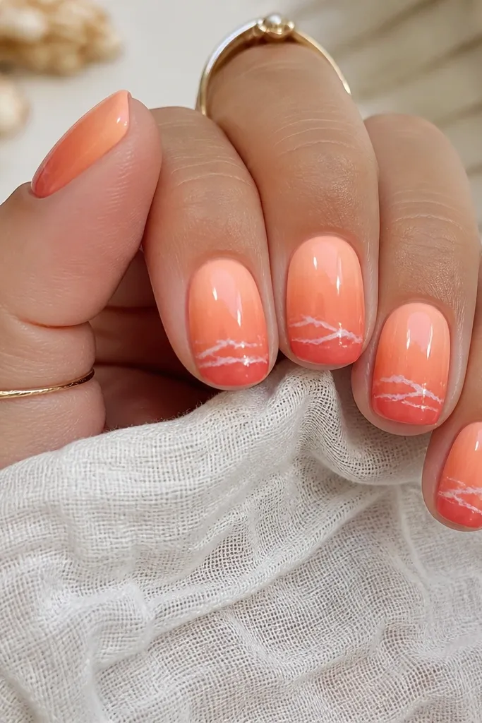 Short squoval nails with a gradient from peach to coral. Near the lower third is a darker orange "waterline" band. Above it are tiny white wave marks, like a shoreline. Glossy finish.
