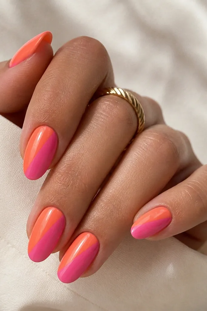 Medium almond nails split diagonally: left side orange-peach, right side warm pink-magenta. The split is a clean diagonal line. Glossy finish.
