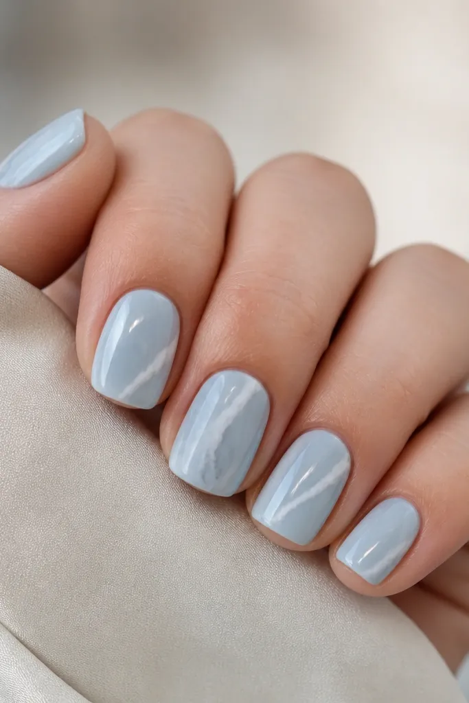 Short squoval nails with a milky sky blue base. Thin white and pale gray veins run diagonally like marble, with one nail having a slightly thicker vein cluster.