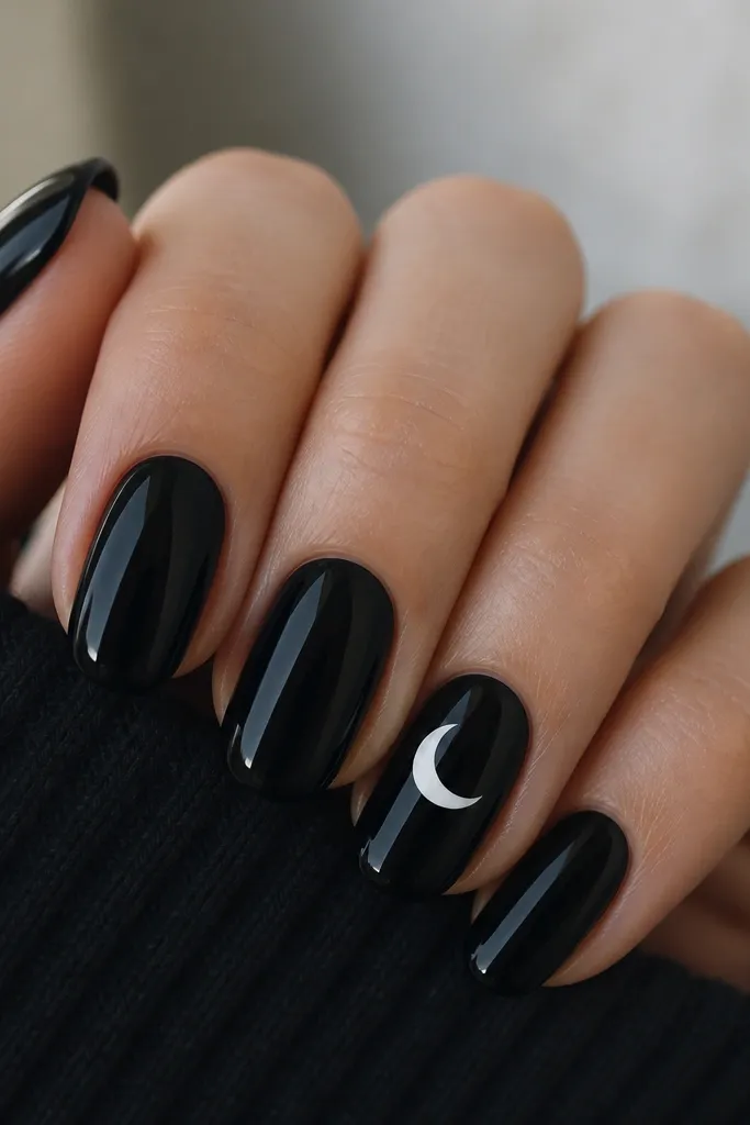 Four nails in deep glossy black. The ring finger has a single white crescent moon placed near the center of the nail, with a clean curved edge. Other nails are plain black with a high shine top coat.