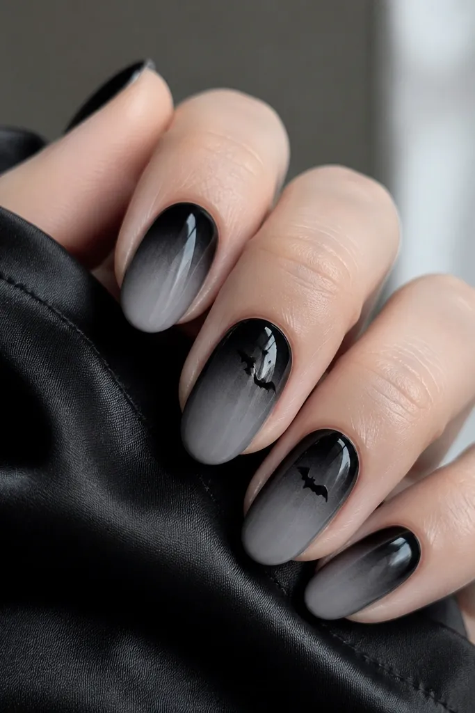 Nails start black at the cuticle and fade into smoky gray toward the tips. On two nails, there are tiny black bat silhouettes near the upper third, drawn as simple V-shapes with small wings.