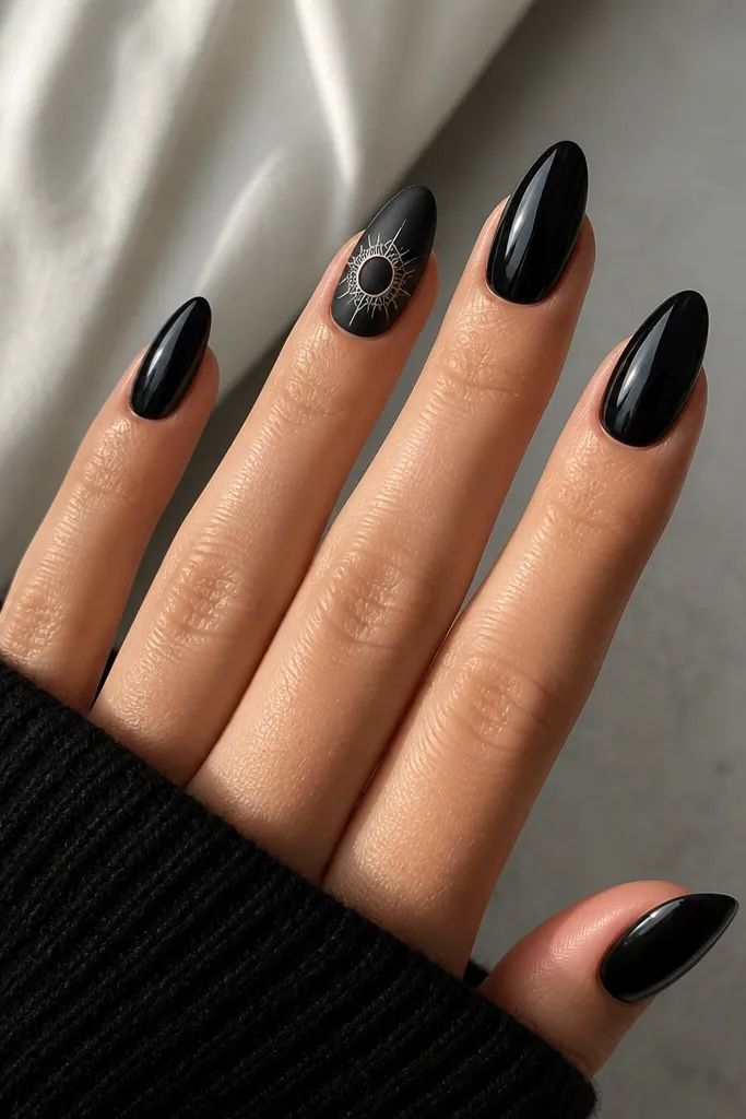 Mostly glossy black nails. The ring finger has a matte finish and a thin spider web drawn around a clear half-moon near the center, like a ring. White lines radiate outward in a neat circle.