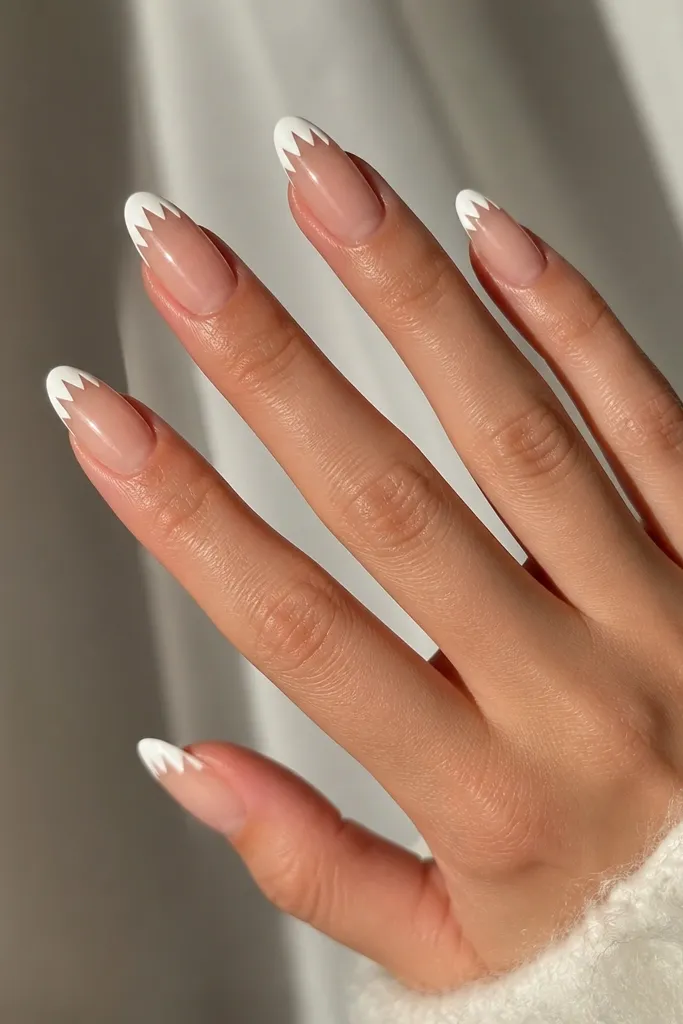 Glossy sheer nails with matte white tips shaped like small teeth - jagged edges across the tip, with a clean cuticle area.